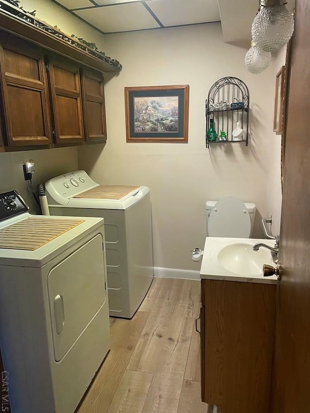 clothes washing area featuring cabinet space, a sink, washing machine and dryer, light wood-style flooring, and baseboards