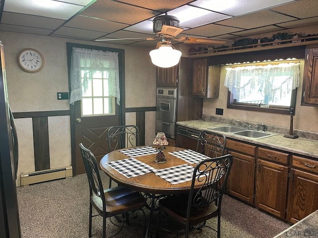 kitchen with a sink, light countertops, baseboard heating, stainless steel double oven, and black dishwasher
