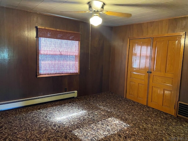 empty room with wooden walls, a ceiling fan, carpet flooring, and baseboard heating