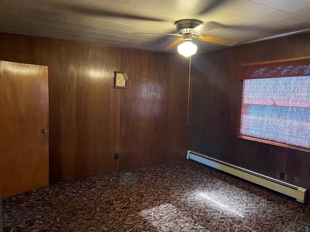 unfurnished room featuring wood walls, a baseboard heating unit, and ceiling fan