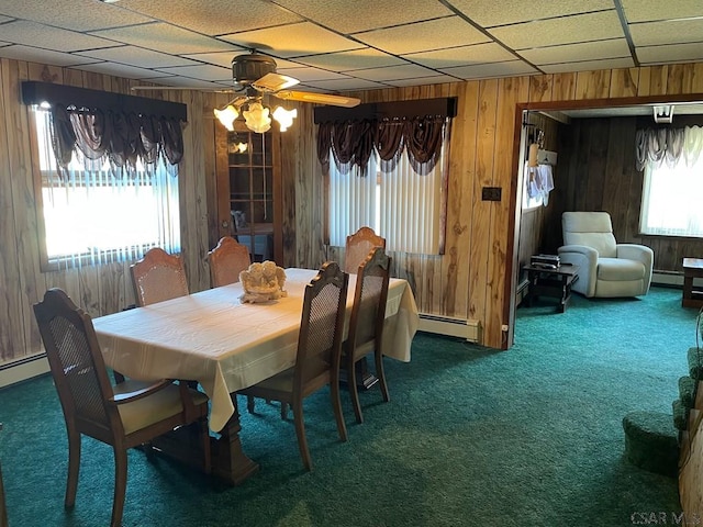 carpeted dining room with wood walls, a ceiling fan, and a baseboard radiator