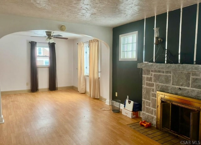 unfurnished living room with a stone fireplace, hardwood / wood-style floors, a textured ceiling, and ceiling fan