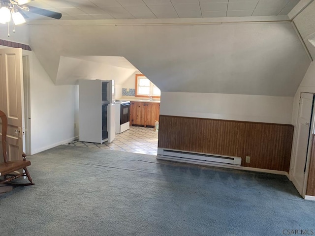 additional living space featuring vaulted ceiling, wooden walls, a baseboard radiator, sink, and light carpet