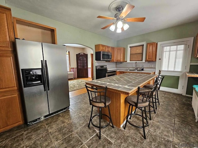 kitchen with sink, a breakfast bar area, appliances with stainless steel finishes, tile counters, and a kitchen island