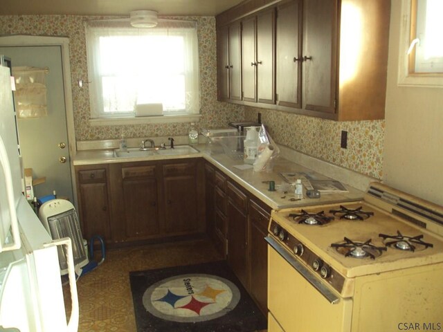 kitchen with white range with gas cooktop, sink, and dark brown cabinets