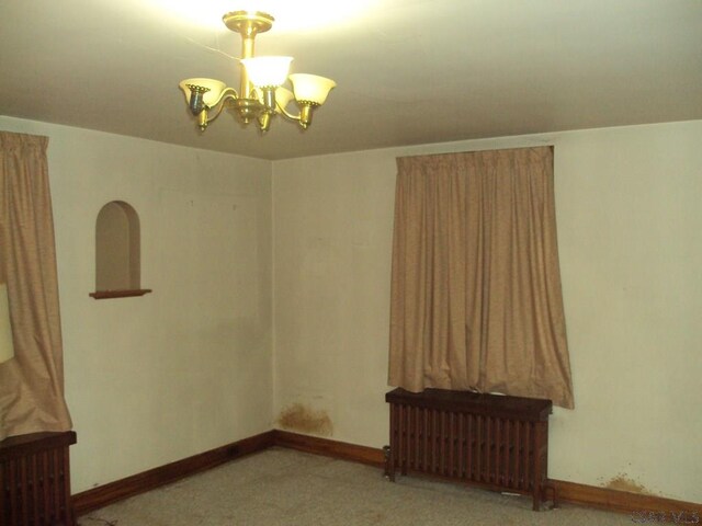 carpeted empty room with radiator heating unit and a notable chandelier