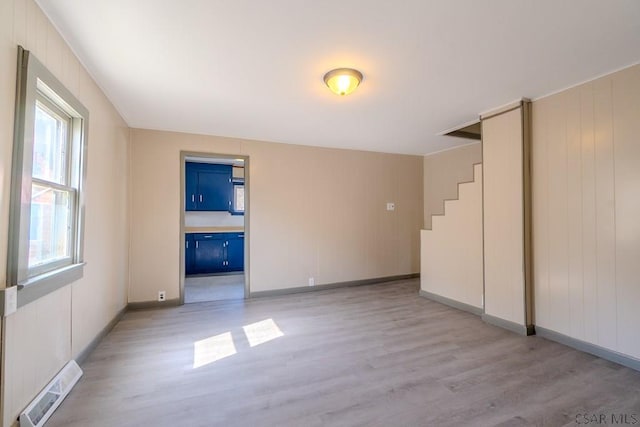 empty room with light wood-style floors, visible vents, and baseboards