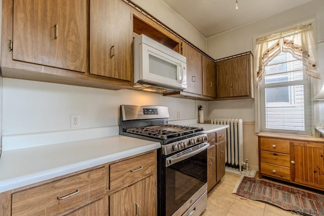 kitchen with light tile patterned floors, stainless steel gas range, radiator, white microwave, and light countertops
