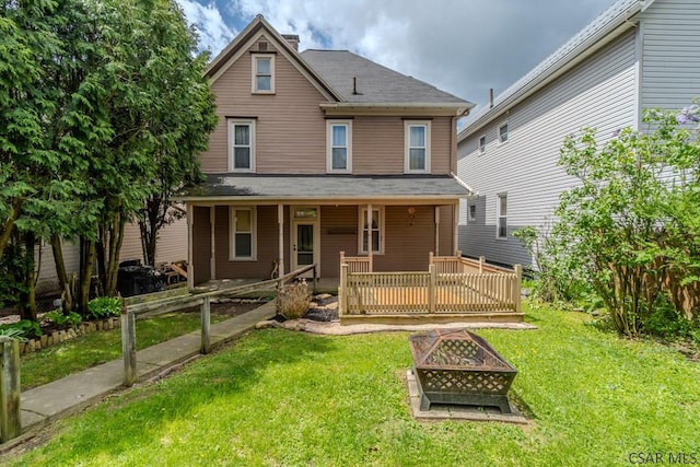 back of property with a yard, a porch, and an outdoor fire pit