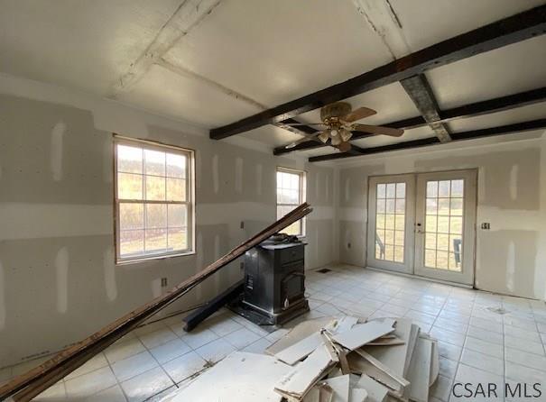 interior space with french doors, coffered ceiling, a wood stove, ceiling fan, and beam ceiling