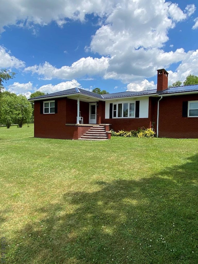 back of house featuring a chimney, a lawn, and brick siding