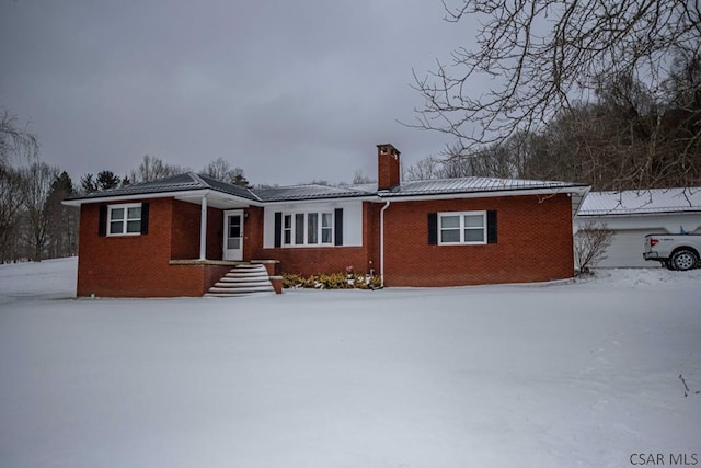 snow covered house featuring a chimney and brick siding