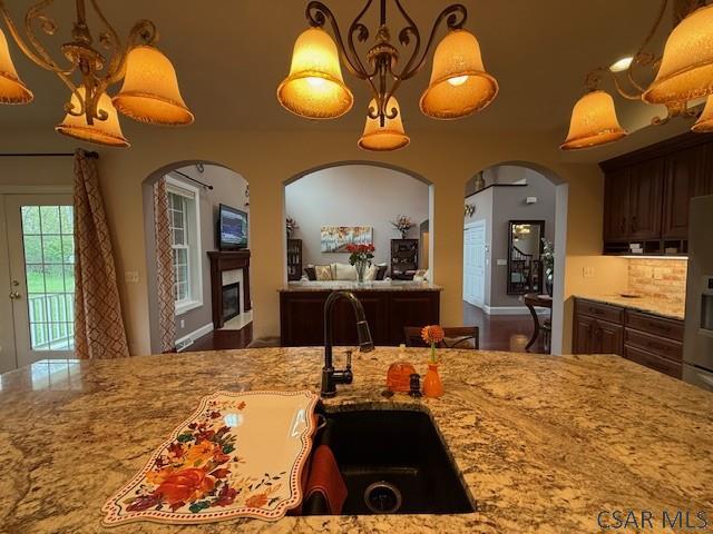 kitchen featuring a sink, light stone counters, a glass covered fireplace, arched walkways, and pendant lighting