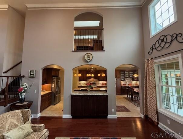 bar featuring freestanding refrigerator, wood finished floors, ornamental molding, plenty of natural light, and a high ceiling