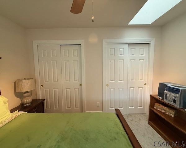 bedroom with multiple closets, a skylight, carpet flooring, and a ceiling fan