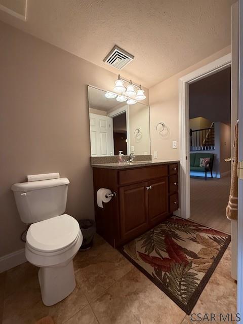 half bathroom with vanity, toilet, a textured ceiling, and tile patterned floors
