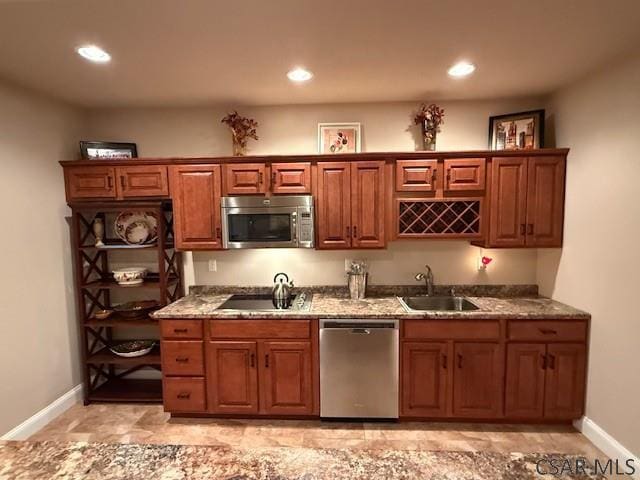 kitchen with appliances with stainless steel finishes, a sink, baseboards, light stone counters, and brown cabinets
