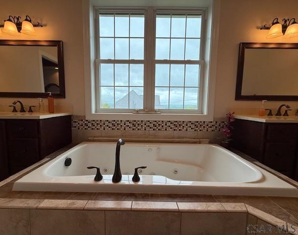 full bathroom with plenty of natural light, two vanities, and a tub with jets