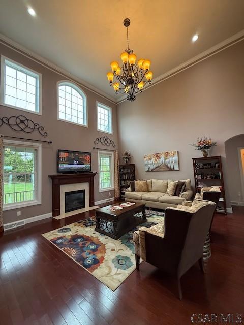 living area with ornamental molding, a chandelier, baseboards, a high ceiling, and dark wood-type flooring