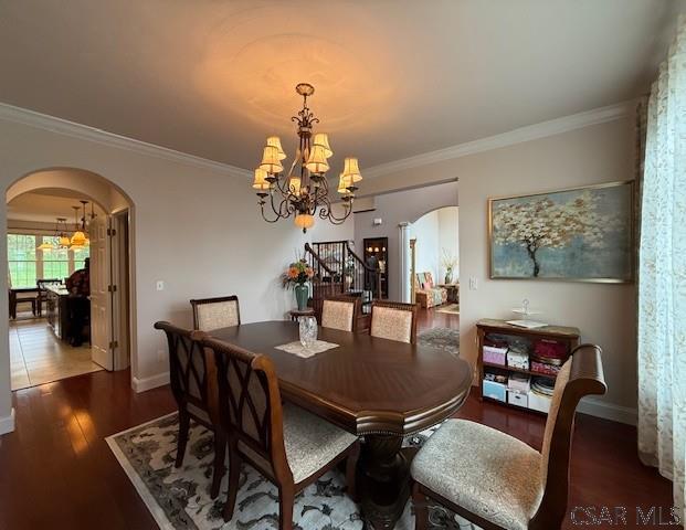 dining space with arched walkways, a chandelier, crown molding, baseboards, and wood finished floors