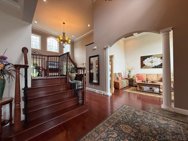 staircase featuring ornate columns, ornamental molding, wood finished floors, baseboards, and a high ceiling