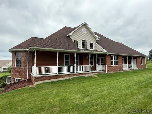 farmhouse featuring a porch, brick siding, a front yard, and a shingled roof