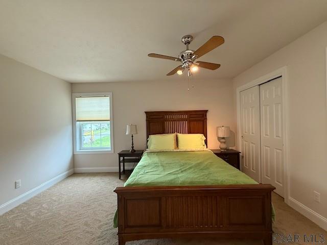 bedroom with baseboards, light colored carpet, a closet, and ceiling fan