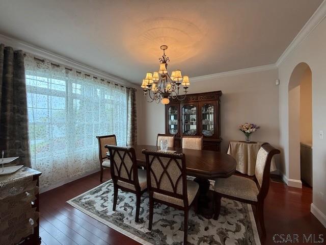 dining space with arched walkways, a chandelier, wood finished floors, crown molding, and baseboards
