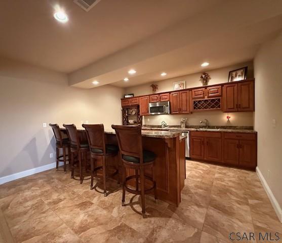 kitchen featuring appliances with stainless steel finishes, a kitchen breakfast bar, baseboards, recessed lighting, and a sink