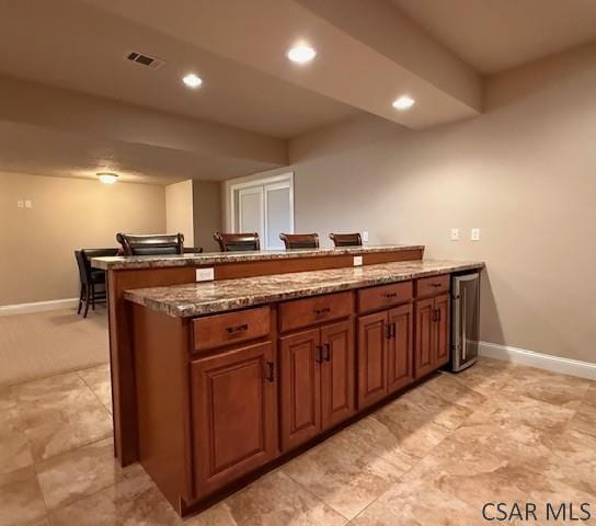 kitchen featuring a peninsula, brown cabinetry, stone counters, baseboards, and recessed lighting