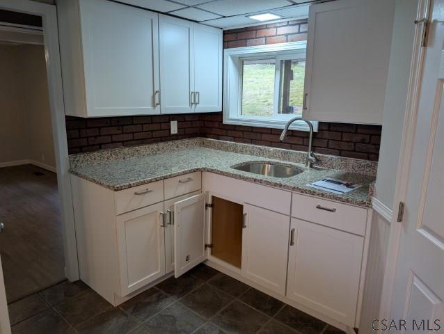 kitchen with backsplash, light stone countertops, sink, and white cabinets