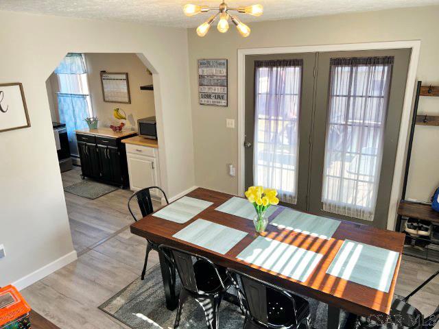 dining area with a textured ceiling, arched walkways, light wood-style floors, an inviting chandelier, and baseboards