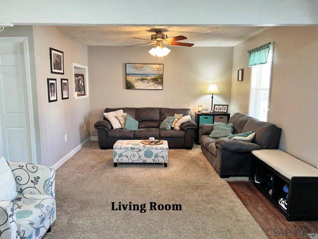 living room featuring a textured ceiling, baseboards, dark carpet, and ceiling fan