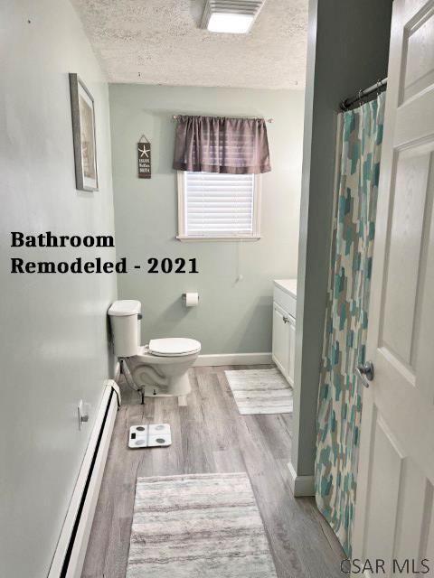 full bathroom with a baseboard heating unit, baseboards, toilet, wood finished floors, and a textured ceiling