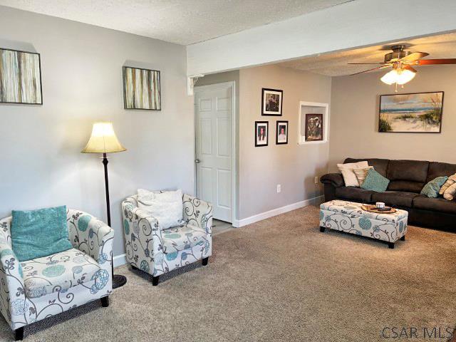 living room featuring baseboards, carpet floors, a textured ceiling, and a ceiling fan