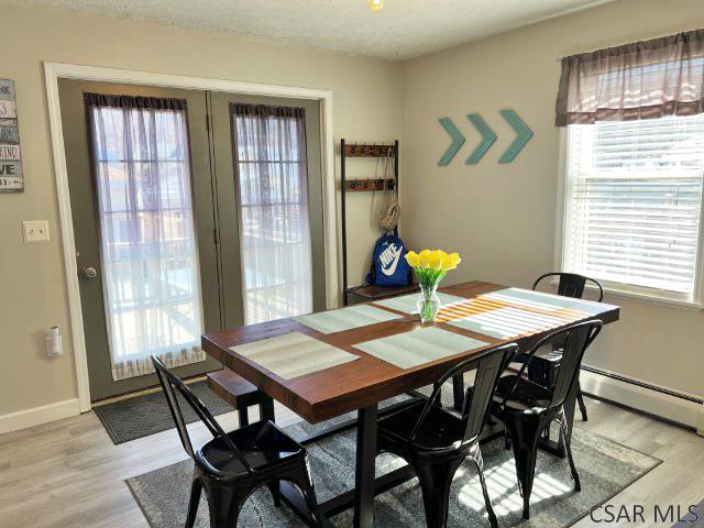 dining area with light wood-style flooring, baseboard heating, baseboards, and a wealth of natural light