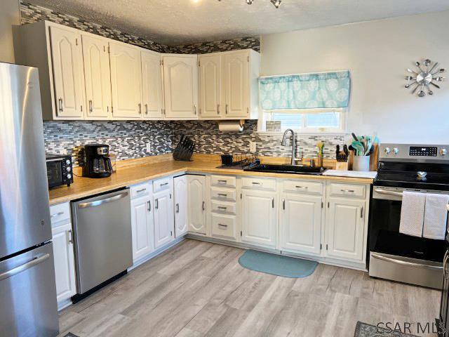 kitchen with a sink, appliances with stainless steel finishes, light wood-style flooring, and white cabinetry