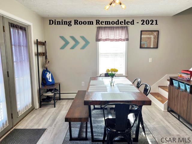 dining area featuring a baseboard heating unit, baseboards, stairway, light wood-type flooring, and a textured ceiling