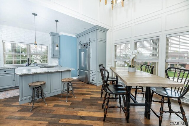 dining space featuring sink, dark wood-type flooring, a wealth of natural light, and a towering ceiling