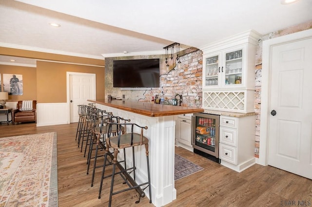 bar featuring white cabinetry, butcher block counters, ornamental molding, beverage cooler, and light wood-type flooring