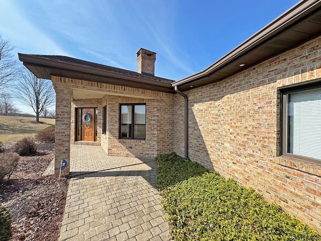 view of exterior entry with a patio, brick siding, and a chimney