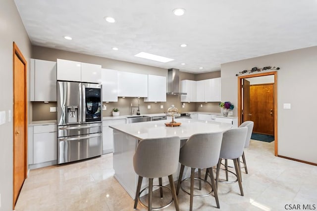 kitchen featuring a breakfast bar, a sink, light countertops, wall chimney range hood, and stainless steel fridge