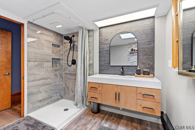 bathroom with vanity, wood finished floors, backsplash, and tiled shower