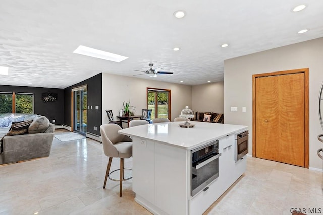 kitchen featuring white cabinetry, a kitchen island, a kitchen bar, black oven, and open floor plan