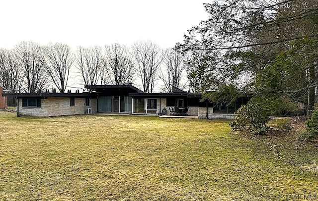 back of house featuring a yard, stone siding, and a patio area