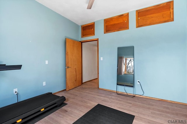 exercise area featuring a baseboard heating unit, ceiling fan, and wood finished floors