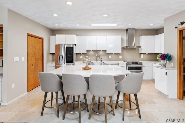 kitchen featuring light countertops, white cabinets, appliances with stainless steel finishes, a kitchen bar, and wall chimney exhaust hood