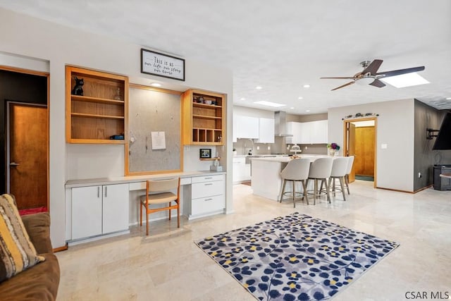 kitchen featuring built in study area, open shelves, white cabinets, a kitchen bar, and wall chimney range hood