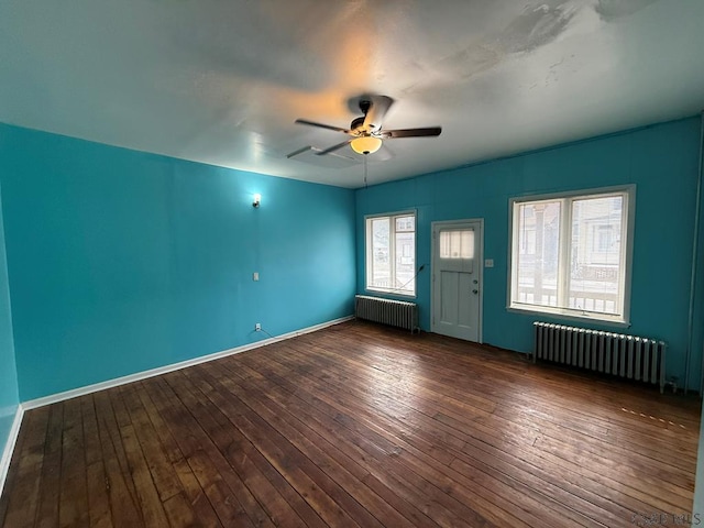 empty room featuring ceiling fan, dark wood-type flooring, baseboards, and radiator