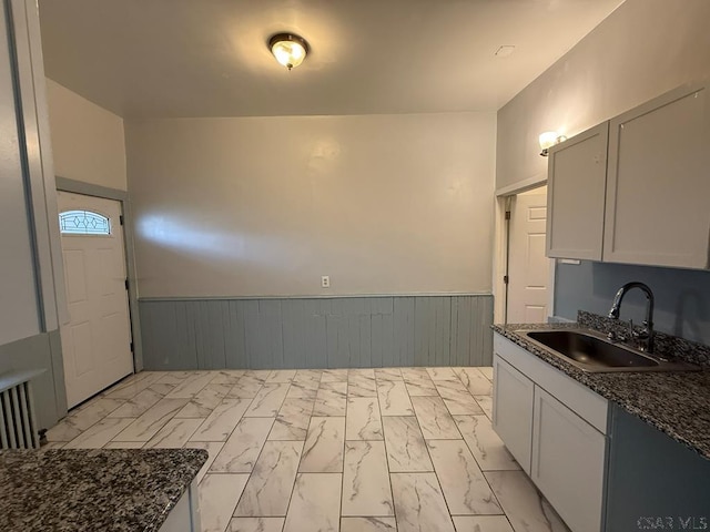 kitchen with dark stone counters, marble finish floor, wainscoting, and a sink